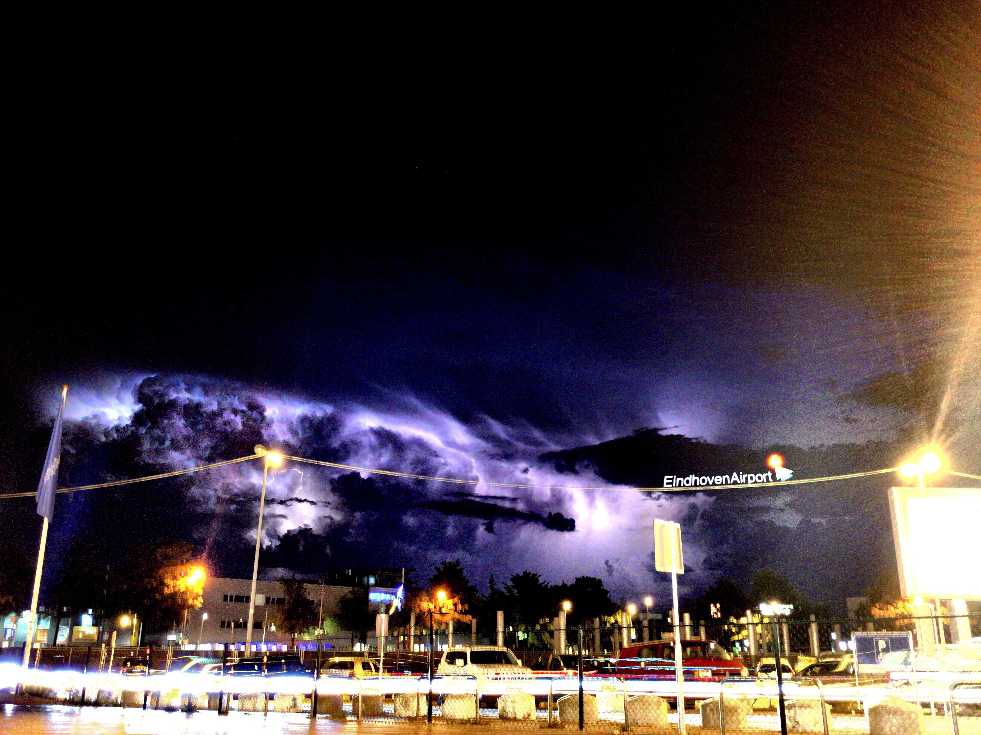 Ominous swollen clouds illuminated by bright purple lightning flashes approaching the airport from the main entrance.